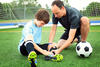 Man helping child soccer player put on equipment.